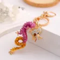 Detailed view of a sparkling rhinestone dragon keychain, stylish metal bag and car key ring. - Violet