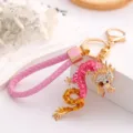 Close-up detail of the pink and gold rhinestone dragon keychain pendant with braided leather strap. - Pink + Leather Cord