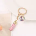 Close-up detail of keychain with pink tassel, gold chain and rhinestone U letter pendant. - Letter U