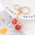 Detailed shot of a sparkling gold heart keychain decorated with clear rhinestones and red flowers. - Color 2