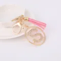 Detailed view of the gold-tone metal keychain featuring a rhinestone letter S and pink tassel. - Letter S