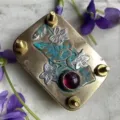 Makroansicht einer Mini-Blumenpresse aus Metall mit Gravuren und einem lila Edelstein-Besatz - Lila / 10 Blatt Papier Inklusive