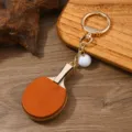Detailansicht des orangefarbenen Tischtennisschläger-Schlüsselanhängers mit Gold-Hardware - Hellbraun