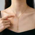 Detailansicht einer eleganten goldenen Y-Halskette mit Quasten aus robustem Titanstahl - Lippen Langer Stab Stil (H1028) / Gold