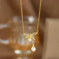 Detaillierte Nahaufnahme einer Halskette mit goldenem Schleifenanhänger und weißen Perlen - Geknotete Perlen-Schleifen-Halskette (9399) / Gold
