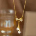 Nahaufnahme einer goldenen Schleifenkette mit Zirkonia und Perlenanhängern. - Perlen-Schleifen-Quasten-Halskette (9391) / Gold