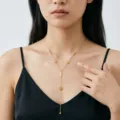 Elegante goldfarbene Y-Halskette mit Rosendetails zu einem schwarzen Trägerkleid. - Langer Stab Kamelien-Quasten Stil (H1190)