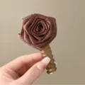 Primo piano dettaglio fiore di rosa in tessuto marrone con elastico per capelli elegante accessorio. - Caffè