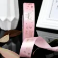 Detail shot of pink satin ribbon featuring gold-stamped birthday cake patterns and text. - Pink