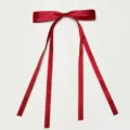 Close-up view of a wine red satin ribbon bow with long hanging tails, smooth fabric detail. - Burgundy