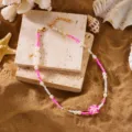 Detail of a colorful beaded beach necklace with a pink plumeria flower pendant on sand. - Single Necklace / Seed Beads Pink