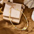 Nahaufnahme einer Perlenkette mit weißer Plumeria-Blüte im Strand-Thema auf Sand - Gelbe Seed Beads