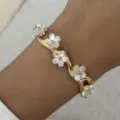 Nahaufnahme eines goldenen gewellten Armreifs mit weißen Perlmuttblumen am Handgelenk - Kirschblüten-Dekoration (BR26Y0311-1) / Gold (Wellenförmiger Floral-Stil)