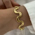 Nahaufnahme eines minimalistischen, vergoldeten, gewellten Edelstahl-Armbands für Damen - Gold (Minimalistischer Wellenförmiger Stil)