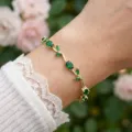 Detailed view of a gold leaf bracelet with green crystals on a wrist. - Gold Green Zirconia