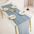 Detailed view of the blue-grey cheesecloth table runner styled on a dining table with plates and candles. - Grey Blue