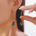 Close-up of golden hoop earrings featuring festive blue enamel Christmas tree charms. - 金色圆环蓝色圣诞树款