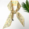 Detailopname van een gele zijden twilly sjaal met bloemenprint en een elegante labeltag. - 1 Gele bloemenprint