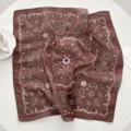 Detailed close-up shot of a brown paisley print square scarf on a white table with cup setup. - 28 Nut Brown Paisley