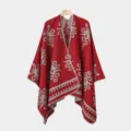 Roter Strick-Herrenponcho mit grauen Blumenmustern an einem Holzkleiderbügel. - Rot