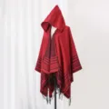 Detailed view of a red hooded knit poncho featuring black stripes and fringe tassels. - 135x150cm / Red