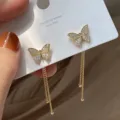 Close-up of butterfly stud earrings with rhinestones and long gold tassels on a card - Butterfly Rhinestone Gold Tassel (ER20Y0876)