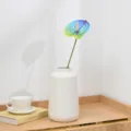 Detail view of an artificial blue anthurium flower in a white ceramic vase on wooden desk. - Teal