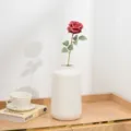 Detailansicht einer künstlichen kurzen Rosenblüte in weißer Keramikvase auf dem Tisch. - Rot