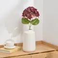 Detail view of artificial hydrangea flower in white ceramic vase on wooden desk. - Burgundy