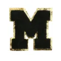 Detailed close-up of letter M patch, black chenille embroidery with gold glitter border. - M