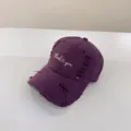 Primo piano di un berretto da baseball viola con testo ricamato e visiera ricurva casuale. - Viola