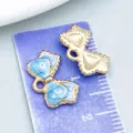 Blue marble enamel bow charm and gold bow pendant displayed on a purple scale ruler - Lake Blue Bow Style (11032) / 1 Piece/Pack (16x10mm)