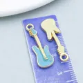 Lake blue enamel and gold alloy guitar charms shown on a purple ruler - Musical Instrument Guitar Style (19455) / 1 Piece (27x9mm)
