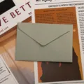 Vue détaillée d'une élégante enveloppe en papier texturé gris-vert sur un vieux journal. - Gris Glacier