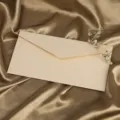Detailansicht eines strukturierten beige Papierbriefumschlags auf goldenem Satin mit Trockenblumen. - Leinenweißer Umschlag (1 Stück)