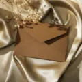 Vue détaillée d'une enveloppe marron vintage texturée en lin posée sur un tissu de soie dorée. - Marron
