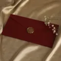 Nahaufnahme eines roten strukturierten Umschlags mit goldenem Wachssiegel und zarten Blumen. - 1 dunkelroter Leinenumschlag + 1 Wachssiegel