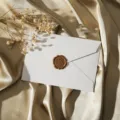 Enveloppe texturée blanche avec sceau de cire vintage et fleurs séchées sur fond satiné doré. - Blanc