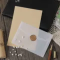 Detailopname van een doorschijnende pergamijn envelop en briefpapier plat op houten bureau. - 3 enveloppen nr. 3 + 10 vellen gelinieerd kraftpapier postpapier + 3 zegellakstempels