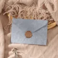 Detailed view of grey textured envelope with bronze wax seal on knit blanket background. - Grey Envelope 1pc + Stamp 1pc