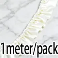 Vue rapprochée d'une bordure plissée en satin blanc, détail d'accessoire de couture. - Beige