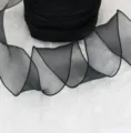 Close-up detail shot of black sheer organza ribbon featuring a graceful wavy presentation. - 6cm 4.5M/Roll / Black