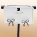 Close-up of sparkling rhinestone bow stud earrings on white display card, elegant jewelry detail. - C-600 Silver