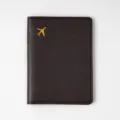 Close-up detail of dark brown PVC leather passport cover with golden airplane stamp motif. - Coffee