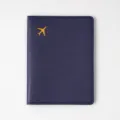 Detailed view of the navy blue passport cover featuring a stylish gold airplane logo. - Dark Blue