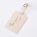 Close-up detail of beige PU leather luggage tag with gold foil text, metal buckle strap. - Off White