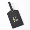 Close-up detail shot of black leather travel luggage tag featuring elegant gold letter K print. - Letter K / Black