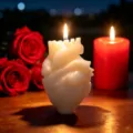 Anatomical heart shaped scented candle detail, warm candlelight on wooden desk with red roses. - White