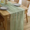 Detailed view of the light green crinkled cheesecloth table runner draped on a wooden table. - 80-300cm Seersucker with Four-Side Rolled Edges / Light Green No. 85