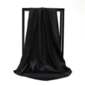 Detailed view of an elegant solid black satin square scarf showing smooth drape and glossy texture. - 90*90cm / Black